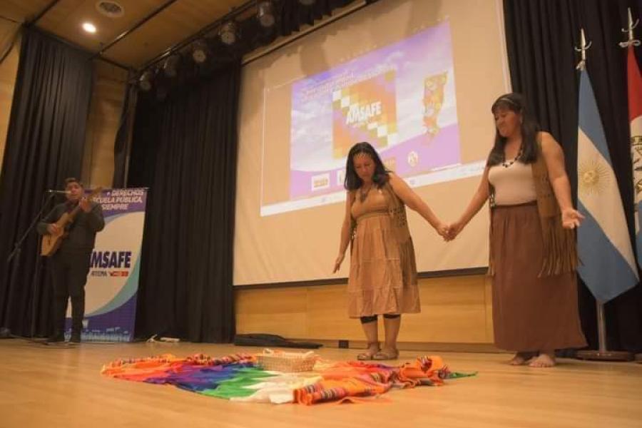 dos mujeres tomadas de la mano en un escenario con un hombre tocando la guitarra y cantando